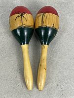 Front view of both maracas showing red tops, scenic artwork, green bands, natural handles
