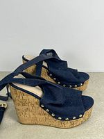 Side view of both denim wedge sandals showing cork soles and studs