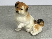 Front view of glazed ceramic dog figurine, seated with paw raised