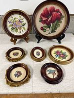 All seven framed needlepoint pieces and two stands arranged on table