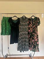 Full view of four green garments hanging on rack: skirt, velvet jumpsuit, floral dress, velvet floral dress