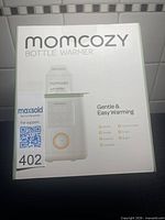 Front of retail box showing Momcozy bottle warmer image and features
