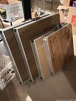 Four folded tables stacked showing laminate tops and aluminum frames
