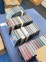 Three stacks of approximately 80–100 jewel-cased CDs on padded mat