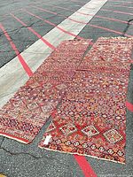 Two red tribal geometric wool runner rugs laid flat, showing pattern, color, fringe, and wear