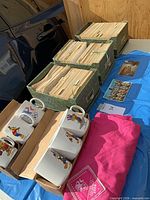 Full lot showing six mugs, three postcard boxes and pink bag