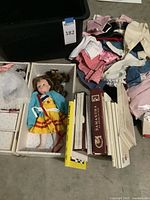 Lot overview showing doll in trunk, pile of clothes, books