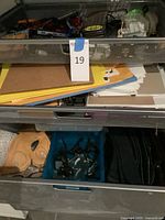 Three mesh drawers showing folders, envelopes, tools, guitar accessories