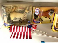 Two boxed Breyer horses (cream palomino and bay) with four small American flags in foreground