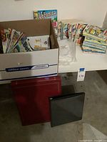 Box of assorted Archie comics beside stack of digests, photo sleeve pack and two binders