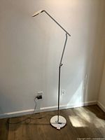 Full view of silver adjustable floor lamp showing base, stem, head, power cord