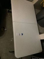 Top view of folded white rectangular table showing center seam and carry handle area