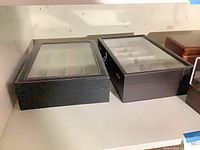 Two black watch display cases with clear tops on shelf