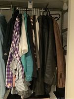 Closet rack with multiple men’s shirts, athletic tops, leather jackets and scarf