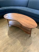 Front angled view of kidney-shaped coffee table showing top, shelf, legs