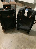 Front view of both black rolling suitcases with leather accents