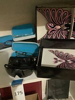 Shelf showing Barbie box, blue eyewear cases, loose sunglasses and eyeglasses
