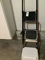 Lot showing black folding ladder, chrome step stool, white plastic stool