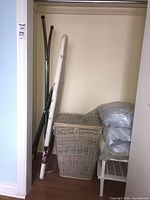 Ironing board, wicker hamper, plastic shoe rack, pillows stored in closet