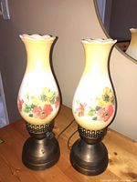 Two floral milk glass hurricane lamps side by side