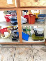 Cabinet shelves holding assortment of plastic containers, pitcher, colander, funnel, skewers