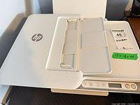 Top view of HP printer showing lid, HP logo and control panel stickered with dimensions