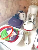 Overall shot showing coffee maker, toaster, hand chopper, kettle, plastic steamers and strainers