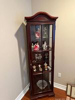 Front view of tall glass curio cabinet with contents inside for scale