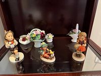 Front view showing three Goebel Hummel figurines and three porcelain flower pieces