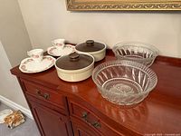 Entire lot displayed on sideboard: two glass bowls, two lidded casseroles, two teacups with saucers
