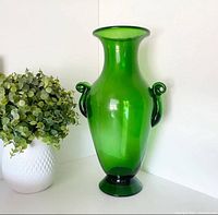 Full view of green glass amphora vase beside plant