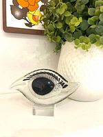 Front view of clear glass eye sculpture with black pupil on acrylic stand