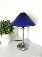 Full view of blue frosted glass lamp beside plant
