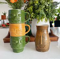 Three stacked Artmark tiki mugs beside larger Westwood tiki mug