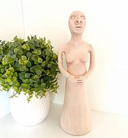 Front view of clay pregnant woman sculpture beside plant for scale