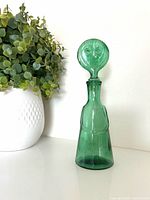Full view of green glass decanter beside plant