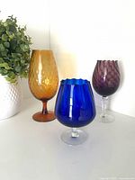 Front view of three Empoli goblets in amber, cobalt blue and amethyst