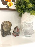 Three owl figurines displayed together: marble, pottery, glass
