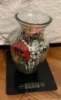 Entire glass vase filled with jewelry on digital scale, weight visible