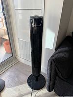 Full view of black tower fan standing on round base