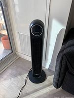 Full view of black tower fan standing on base with power cord