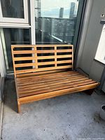 Full view of wooden patio loveseat frame placed on balcony concrete floor, shows overall construction and finish