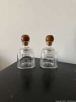 Two clear glass Patron-style bottles with wood stoppers front view