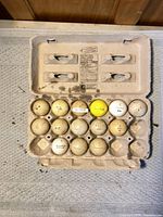 Egg carton containing 14 vintage golf balls with varied markings
