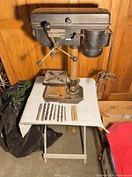 Front view of Jobmate drill press on stand with drill bits and ruler laid out