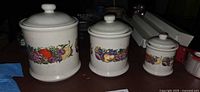 Front view of three graduated ceramic canisters with fruit band and lids