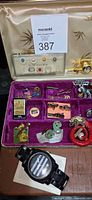 Open jewelry case showing tacs, pins, cufflinks, airplane clock and wristwatch