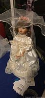 Full view of bridal doll on stand wearing satin gown and veil