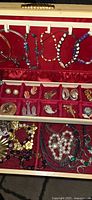 Open jewelry box showing red velvet interior with bracelets on hooks and compartmented tray of assorted jewelry
