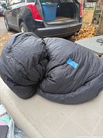 Rolled dark gray adult sleeping bag on table, blue brand tag visible
